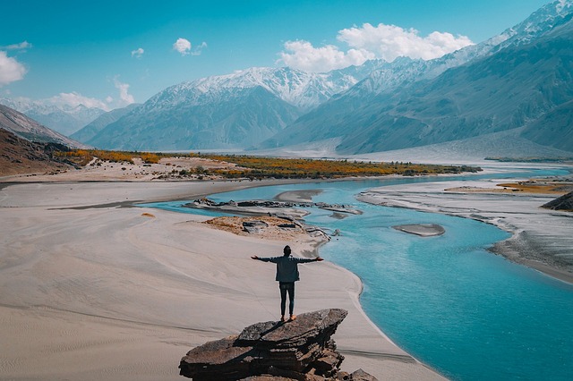 Person steht auf einem Felsvorsprung mit Blick über Fluss und Berge